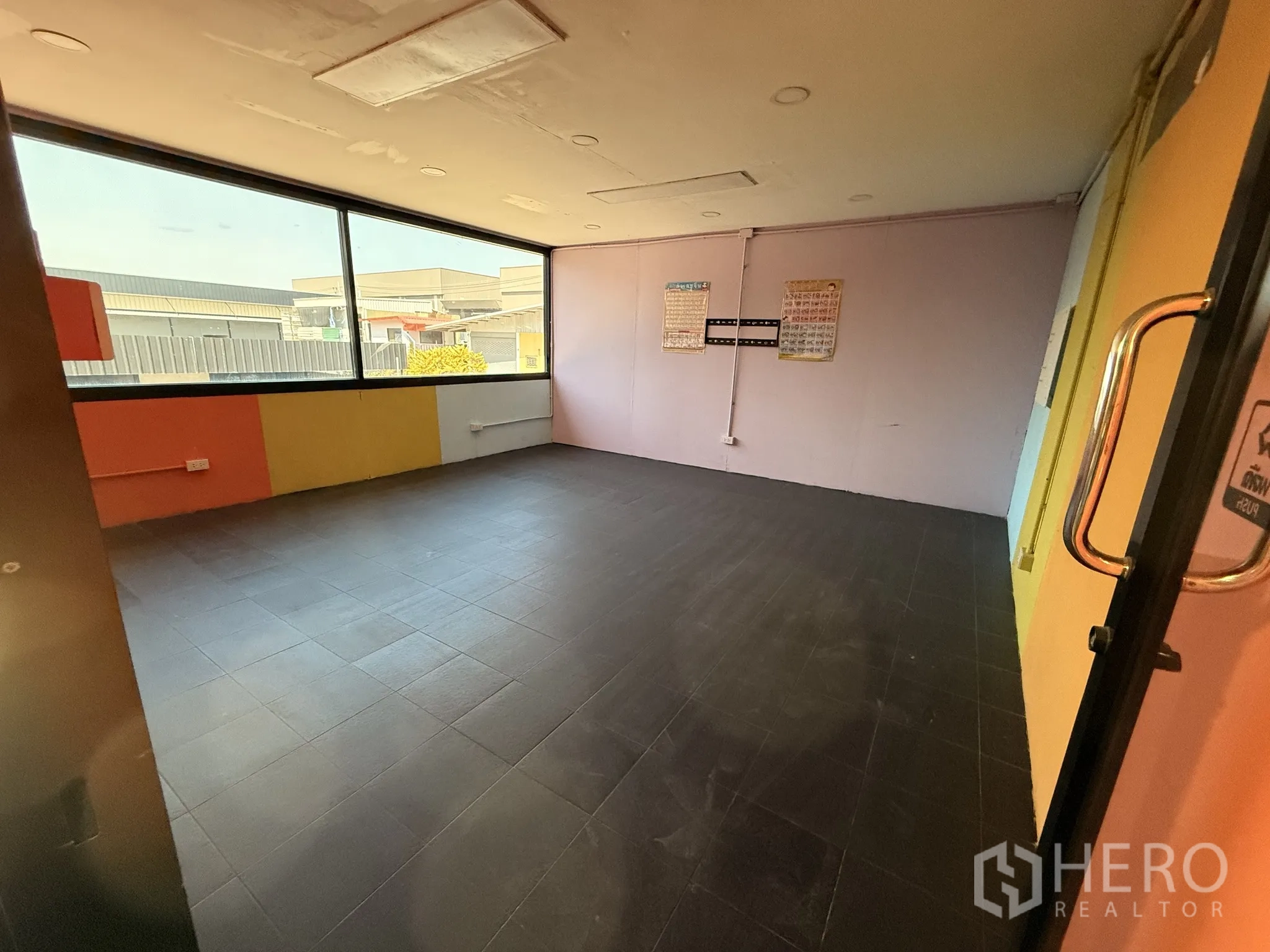 Warehouse for rent in Lat Krabang, Bangkok - Second-floor multipurpose room with dark floor tiles, pastel walls, and a wide window.