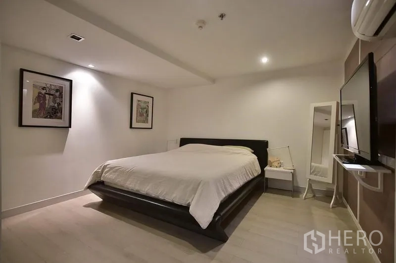 Condominium for rent in Khlong Toei, Bangkok - Master bedroom with king bed, wall-mounted TV, mirror and air conditioning.