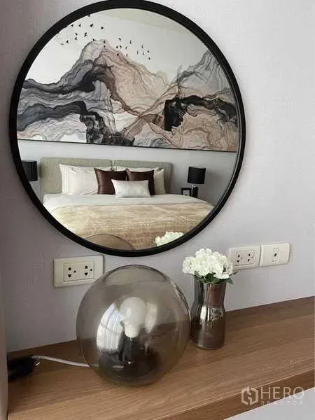 Condominium for rent in Pathum Wan, Bangkok - Round mirror above console reflecting the bedroom with art headboard and neutral decor.