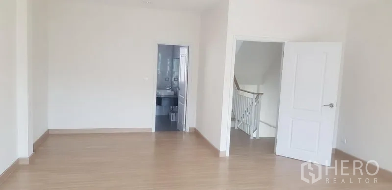 Townhouse for rent in Bang Na, Bangkok - Large bedroom with light wood floors, white doors, and access to an ensuite bathroom.