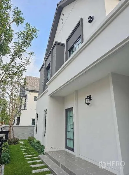 Detached House for rent in Bang Phli, Samut Prakan - Side exterior view with stepping-stone path, green lawn and glass entry door.