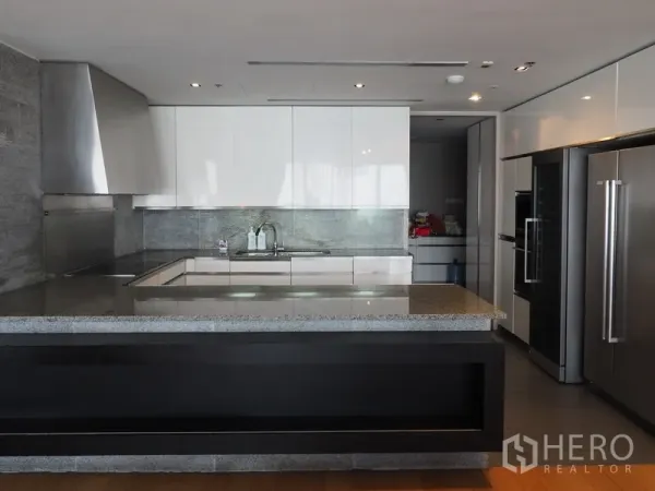 Condominium for rent in Sathon, Bangkok - Modern U-shaped kitchen with stone island, stainless appliances and glossy white cabinets.