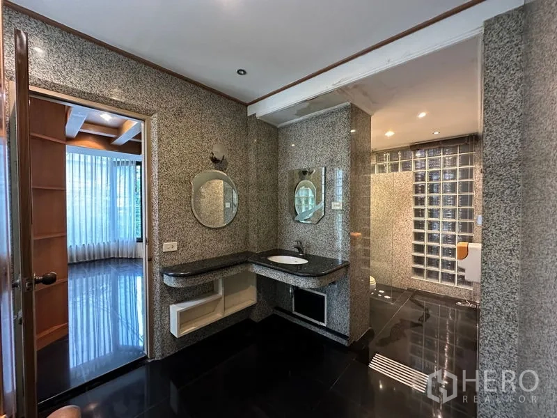 Townhouse for rent in Khlong Toei, Bangkok - Granite-clad bathroom with glass-block shower, round mirrors and black tile flooring.