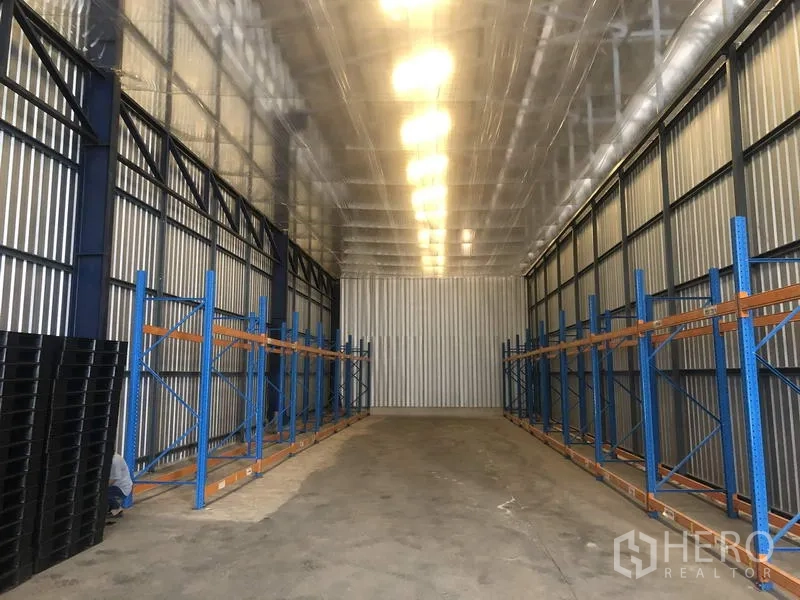 Warehouse for rent in Pak Kret, Nonthaburi - High-ceiling warehouse aisle with blue steel racking and an insulated metal roof in Pak Kret, Nonthaburi.