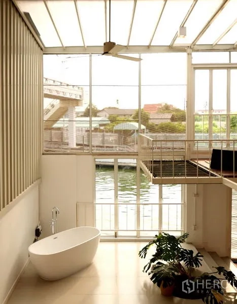 Townhouse for rent in Khlong Toei, Bangkok - Atrium space with large windows overlooking a canal and a freestanding bathtub, creating a serene corner.