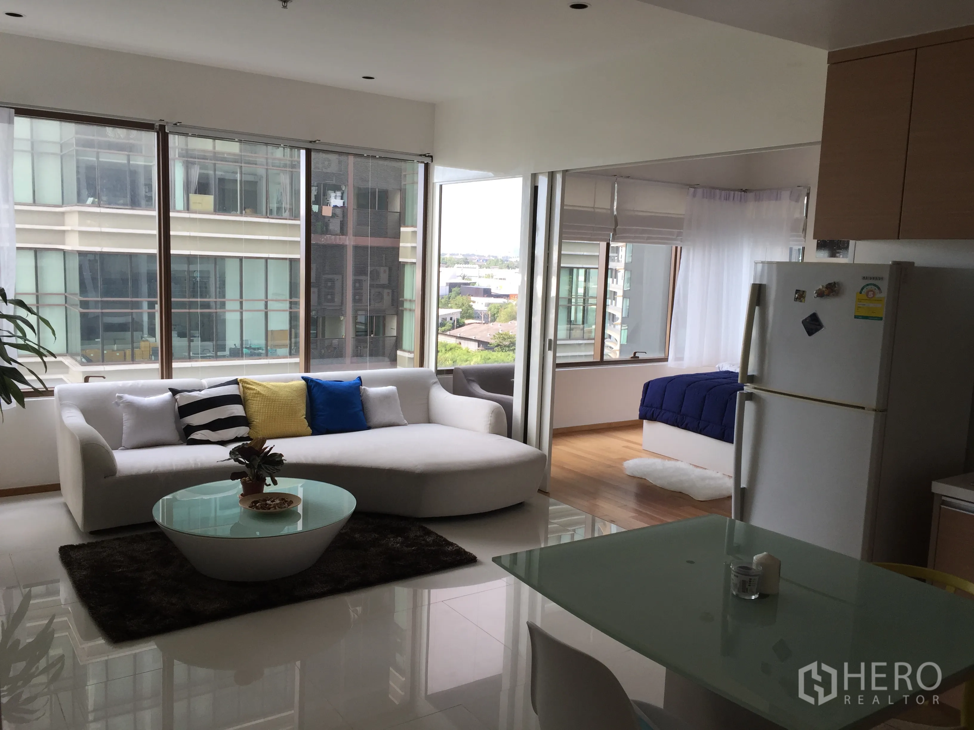 Condominium for rent in Khlong Toei, Bangkok - Bright open‑plan living area with white sofa, glass coffee table, dining corner and large windows with city views.