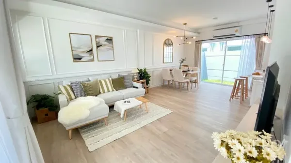 Townhouse for rent in Prawet, Bangkok - Spacious lounge with sectional sofa, wall moulding, dining set and full-height windows bringing in natural light.