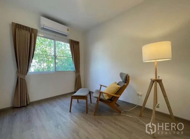 Townhouse for rent in Prawet, Bangkok - Cozy reading corner with lounge chair, ottoman, and floor lamp by window