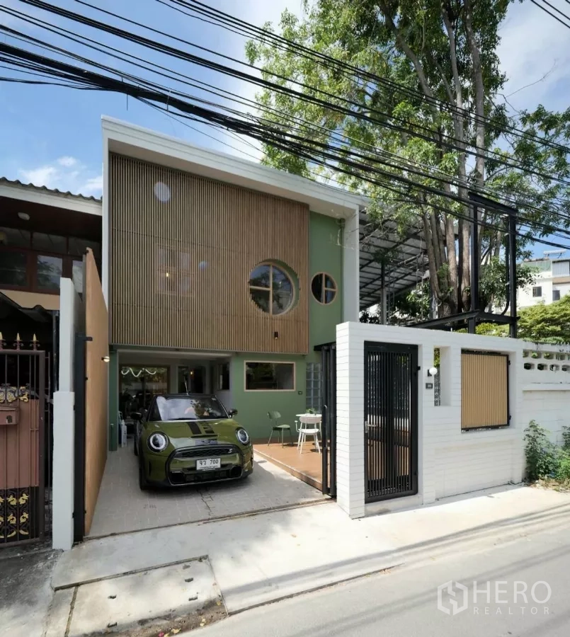 联排别墅 出租在Watthana, Bangkok - 白天外观，车库车位、圆窗与木百叶立面、白色砖墙与滑动门。
