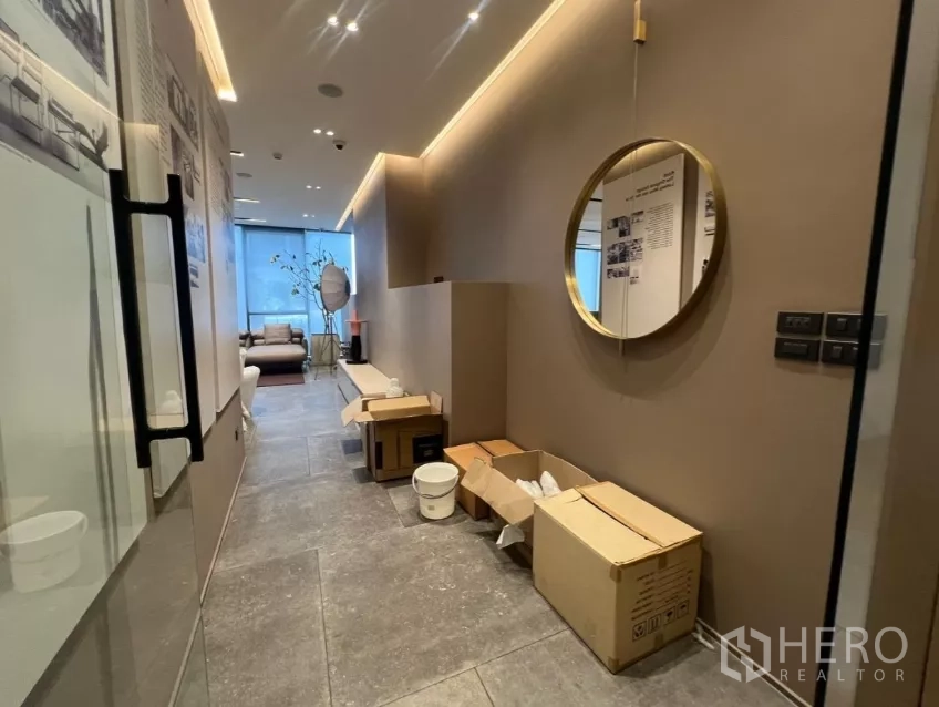 Retail Space for rent - Entrance corridor with glass door, round mirror and boxes on stone tiles leading to the main retail area.