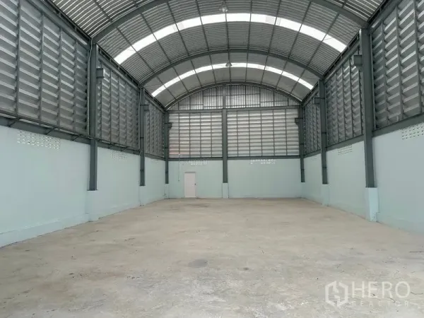 Factory for rent in Pak Kret, Nonthaburi - Spacious factory hall with high arched roof, ventilated metal panels and reinforced concrete floor.