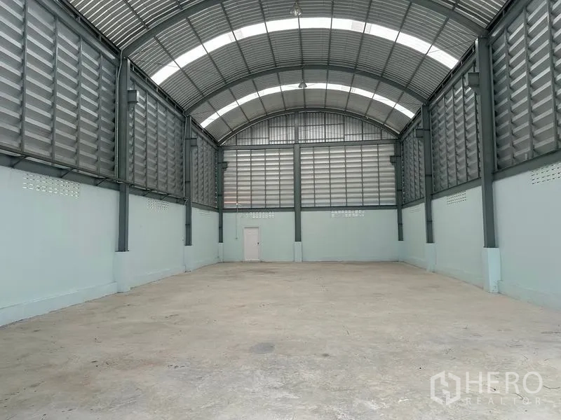 Factory for rent in Pak Kret, Nonthaburi - Spacious factory hall with high arched roof, ventilated metal panels and reinforced concrete floor.