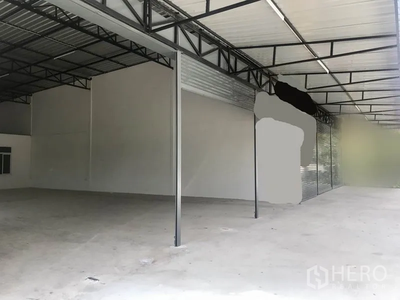 Warehouse for rent in Lam Luk Ka, Pathum Thani - Covered loading area with steel trusses, high roof and concrete floor, featuring long roller doors.