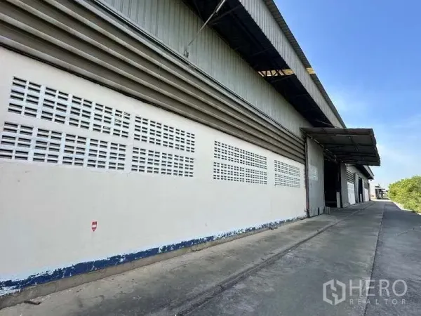 Warehouse for rent in Wang Noi, Phra Nakhon Si Ayutthaya - Side elevation of the warehouse showing ventilation block walls and a sheltered loading dock along a concrete driveway.