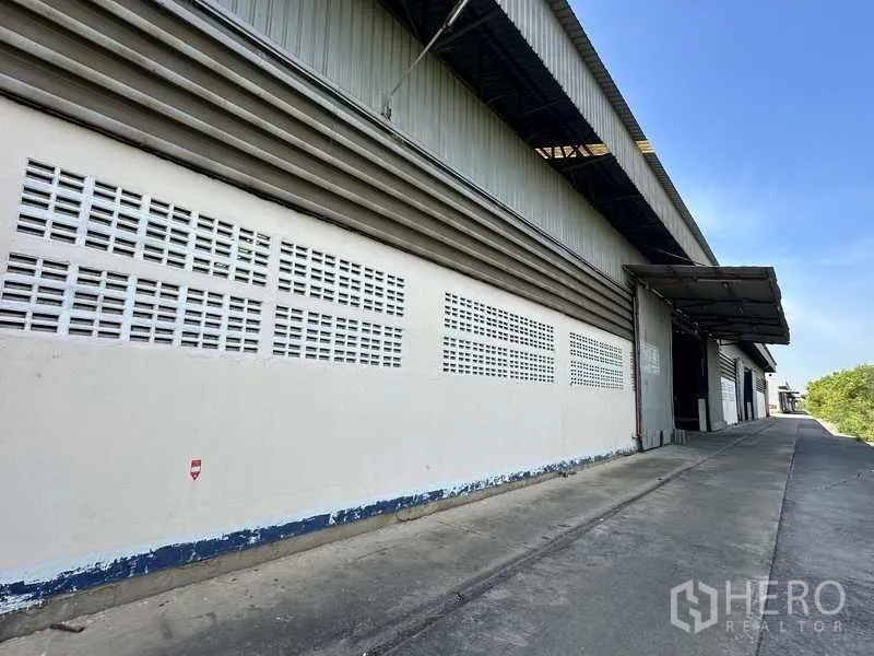 Warehouse for rent in Wang Noi, Phra Nakhon Si Ayutthaya - Side elevation of the warehouse showing ventilation block walls and a sheltered loading dock along a concrete driveway.