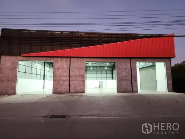 货栈 出租在Pak Kret, Nonthaburi - 夜间立面，三处照明充足的装卸口与红色檐板醒目。