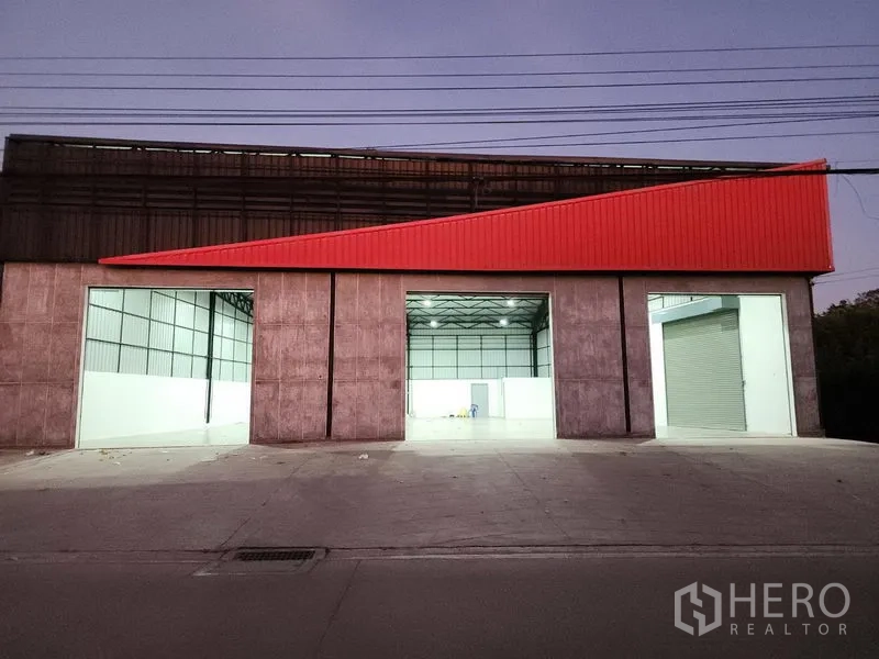 货栈 出租在Pak Kret, Nonthaburi - 夜间立面，三处照明充足的装卸口与红色檐板醒目。