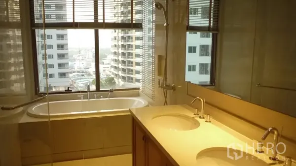 Condominium for rent in Khlong Toei, Bangkok - Bathroom with large window, soaking tub, glass shower and double-sink vanity.