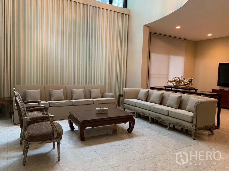 Detached House for rent or sale in Khan Na Yao, Bangkok - Formal living room with double-height curtains and classic sofas around a table.