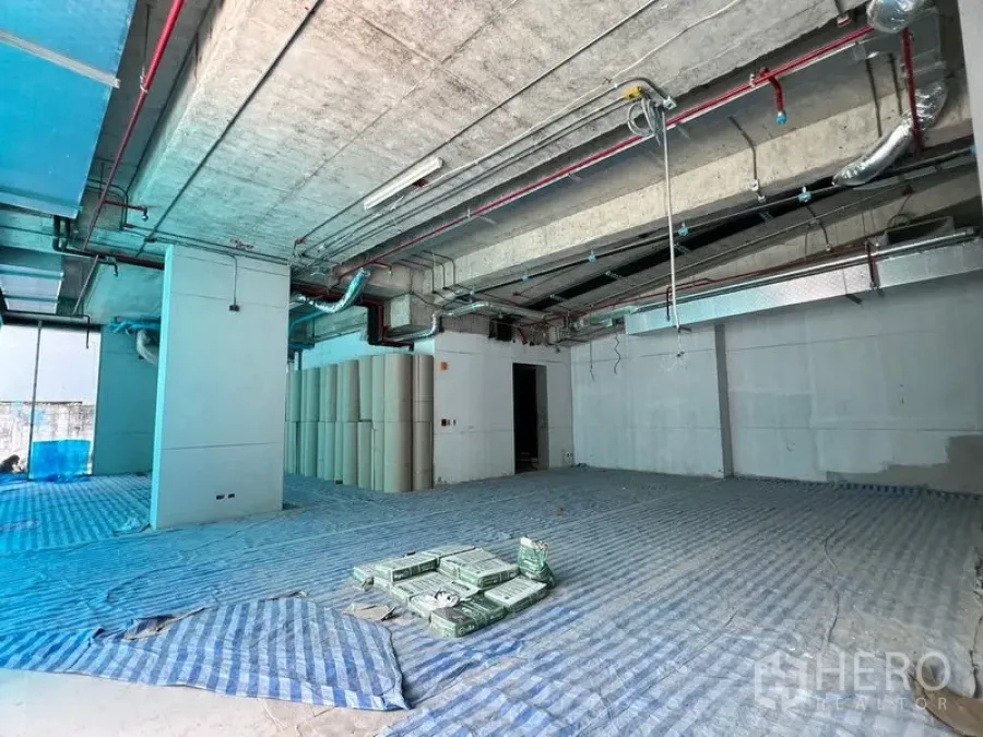Retail Space for rent in Khlong Toei, Bangkok - Open-plan retail shell with exposed concrete ceiling, ducts, and blue floor protection.