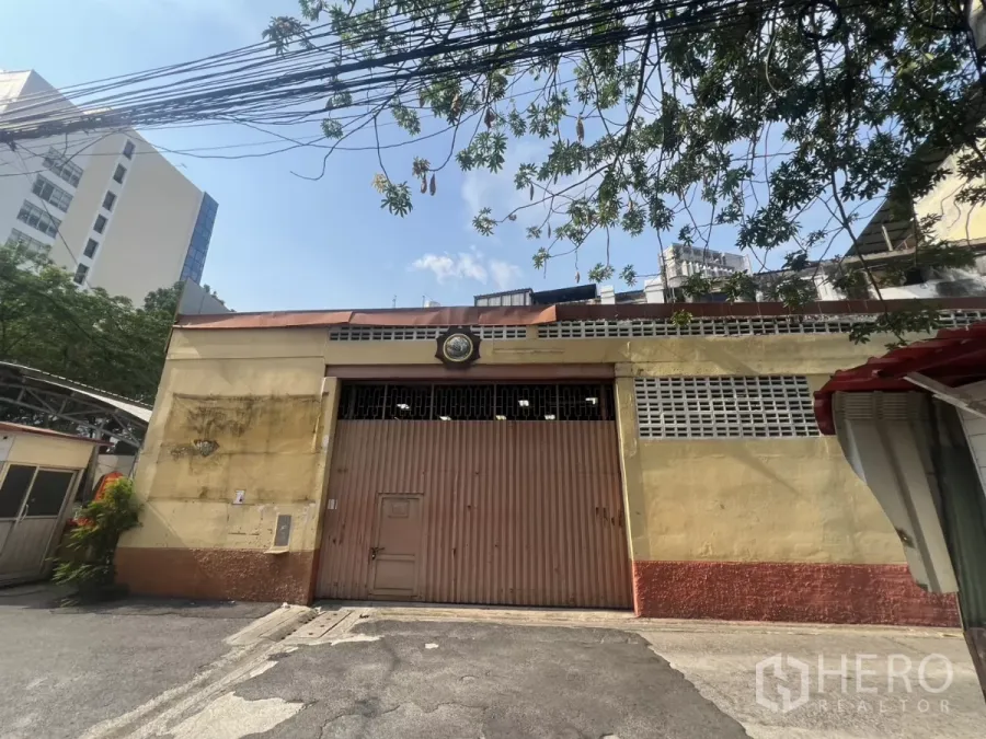 Warehouse for rent in Khlong Toei, Bangkok - Exterior of a single-storey warehouse with a wide steel gate and ventilation blocks in Khlong Toei.
