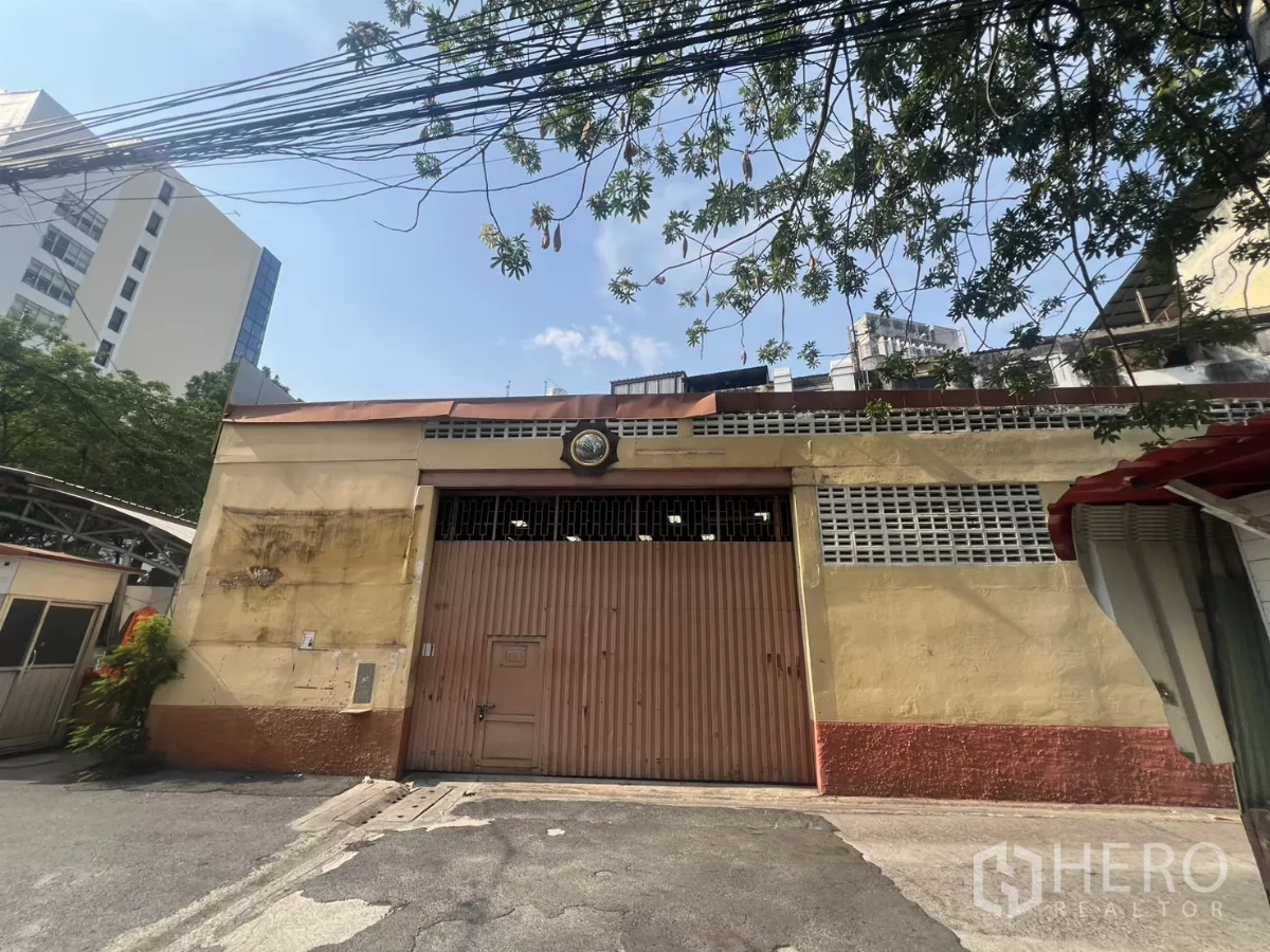 货栈 出租在Khlong Toei, Bangkok - 空堤区仓库外观，带大型钢制卷闸门与通风砖墙。