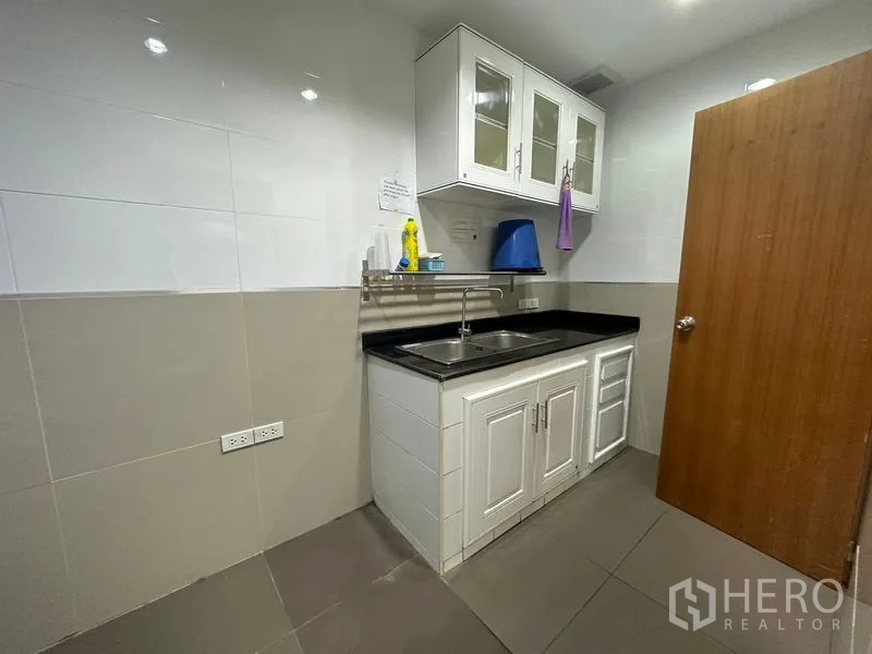 Office Space for rent or sale - Compact pantry with white cabinets, black countertop and sink.