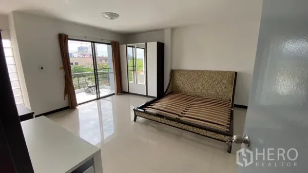 Townhouse for rent in Bang Na, Bangkok - Bright master bedroom with sliding glass doors to a balcony and a bed frame.