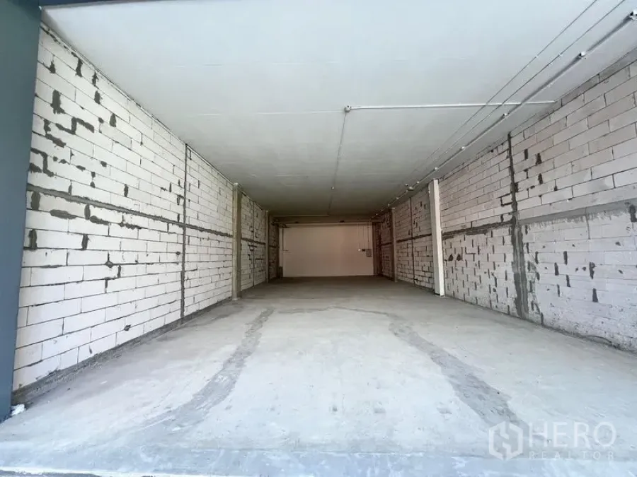 Retail Space for rent - Empty unfinished retail unit with concrete floor, white block walls and ceiling lights in a deep rectangular layout.
