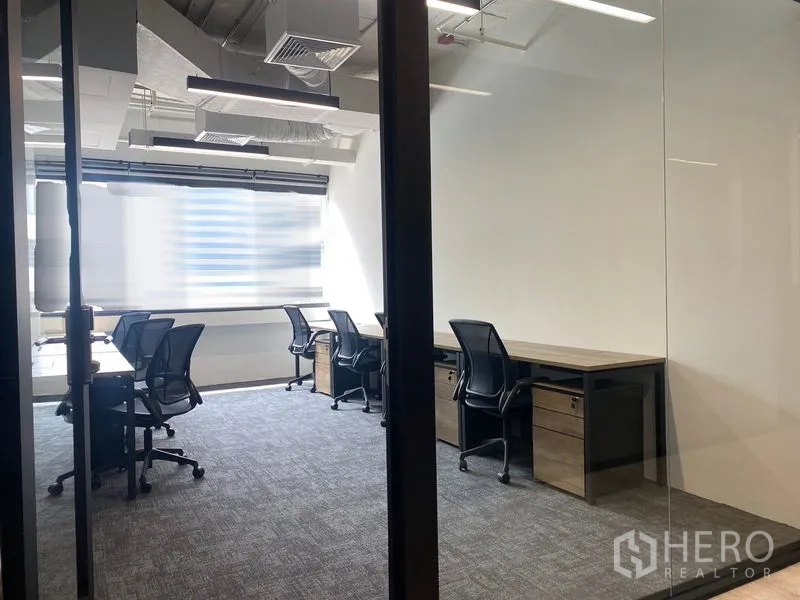 Office Space for rent in Bang Rak, Bangkok - Glass-partitioned workspace with rows of desks, carpet flooring and under-desk pedestals.