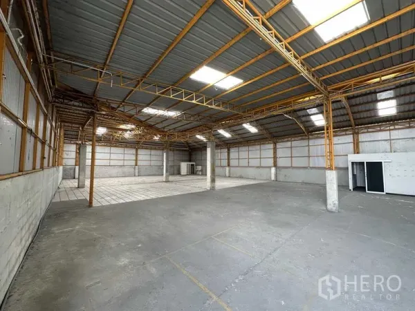 Warehouse for rent in Mueang Pathum Thani, Pathum Thani - Open warehouse interior with high steel truss roof, skylights, and a concrete floor with a tiled section.