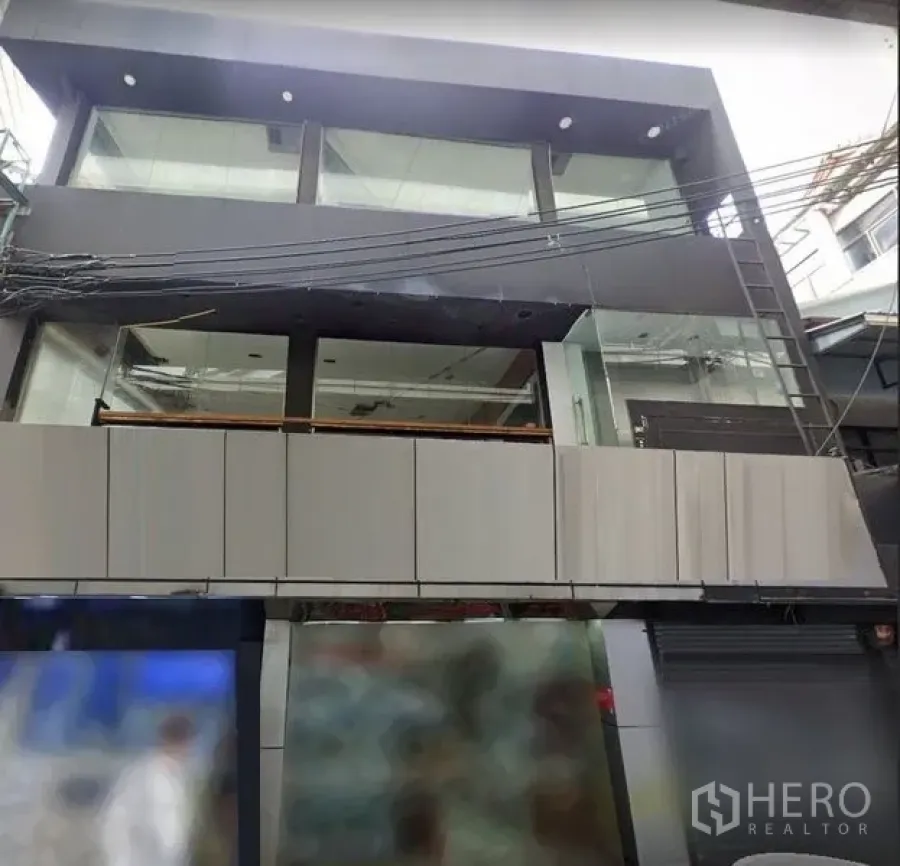 Shophouse for rent in Khlong Toei, Bangkok - Contemporary multi-storey shophouse facade with full-height glass windows above a busy urban street.