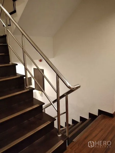 Shophouse for rent in Watthana, Bangkok - Staircase with dark wood steps and stainless-steel handrail in the common area.