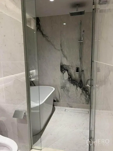Condominium for rent in Pathum Wan, Bangkok - Luxury marble bathroom with glass rain shower and freestanding bathtub.