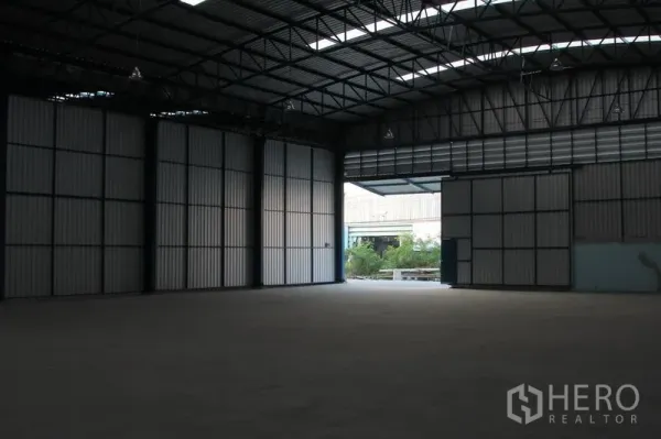 Warehouse for rent in Lat Krabang, Bangkok - Interior view toward open doors showing driveway access and greenery outside the Lat Krabang warehouse.