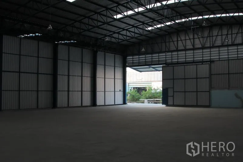 Warehouse for rent in Lat Krabang, Bangkok - Interior view toward open doors showing driveway access and greenery outside the Lat Krabang warehouse.