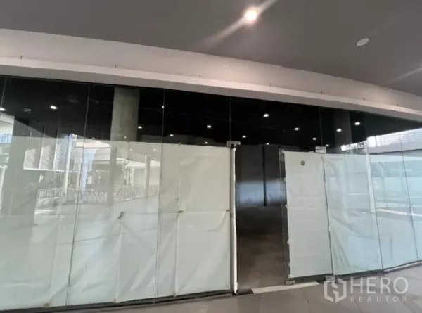 Retail Space for rent - Front view of the vacant shop with full-height glass doors and black fascia inside a shopping complex.