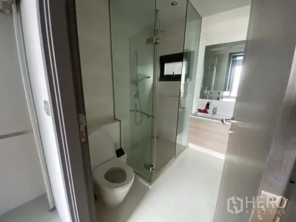 Condominium for rent in Khlong Toei, Bangkok - Contemporary bathroom with glass-enclosed shower, toilet and vanity with mirror