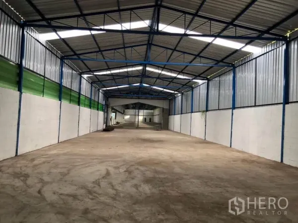 Factory for rent in Nonthaburi - Secondary factory bay with steel frame roof, green ventilated panels and open concrete floor.
