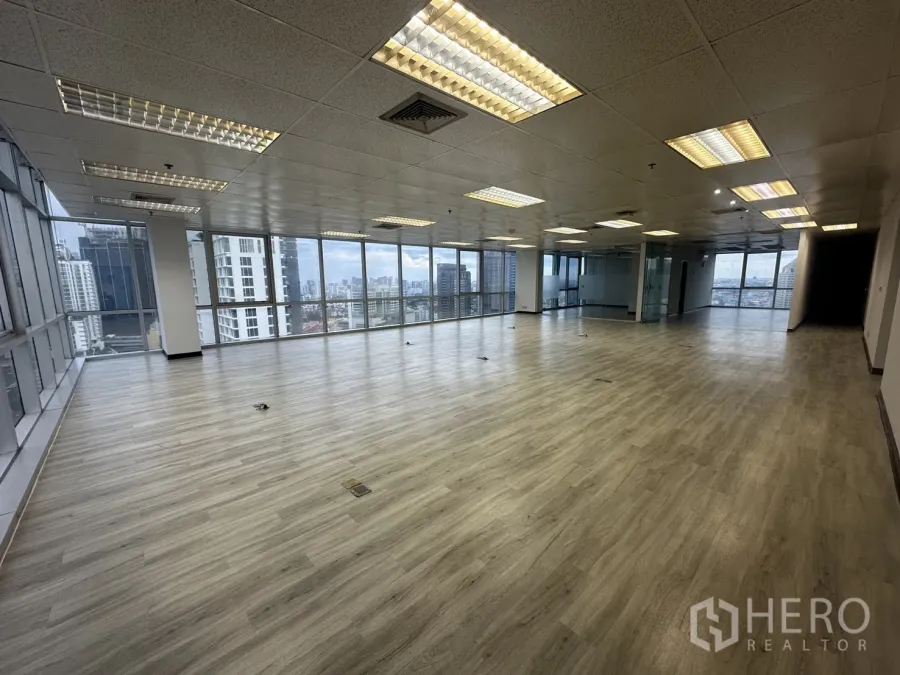 Office Space for rent - Open-plan 226 sqm office with wood-look floors, grid ceiling lights and panoramic Bangkok skyline through full-height windows.