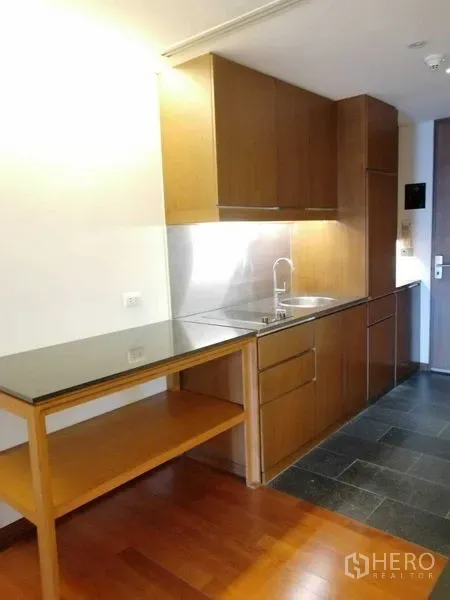 Condominium for rent in Pathum Wan, Bangkok - Compact kitchenette with wood cabinets, stone countertop and stainless backsplash.
