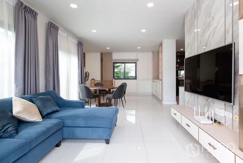 Detached House for rent in Bang Phli, Samut Prakan - Open-plan living and dining area with blue sectional sofa, TV wall and recessed lighting.