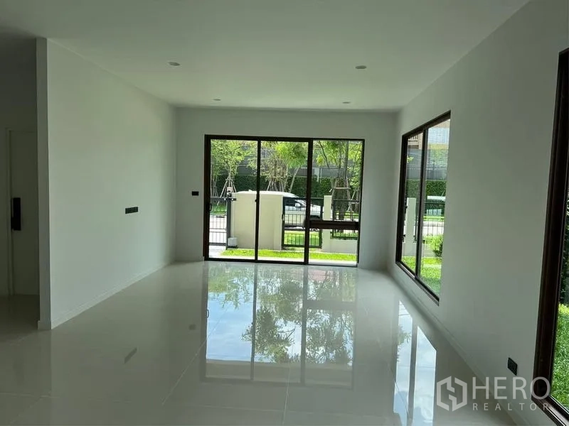 Detached House for sale in Bang Kapi, Bangkok - Living area with glossy tiled floors and sliding glass doors opening to the garden.