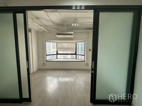 Office Space for rent in Pathum Wan, Bangkok - Open office behind sliding frosted glass doors with exposed ceiling pipes and a wide bay window.