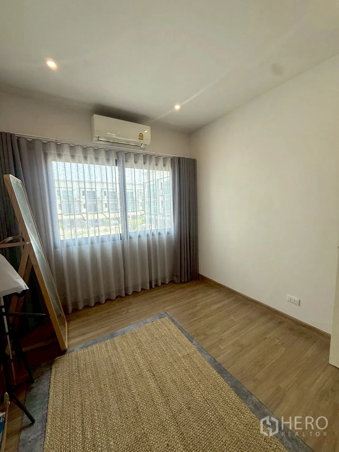 Townhouse for rent in Prawet, Bangkok - Bedroom with wood flooring, large window, curtains and wall-mounted air conditioner.
