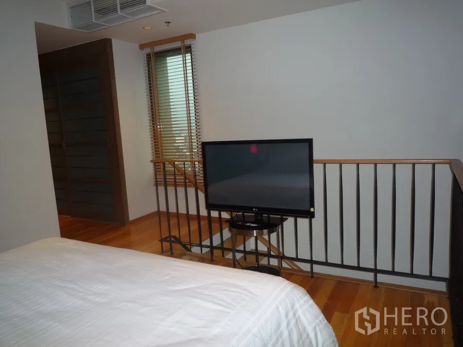 Condominium for rent in Khlong Toei, Bangkok - Mezzanine bedroom with TV at the foot of the bed, railing and window blinds.