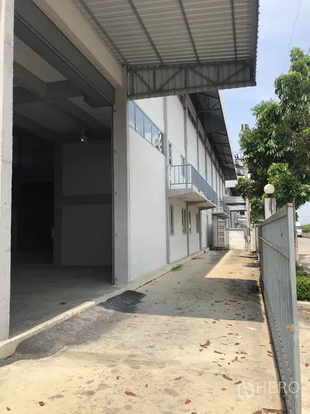 Factory for rent in Lam Luk Ka, Pathum Thani - Entry side of the factory with tall roller door, small balcony, windows and front fence.