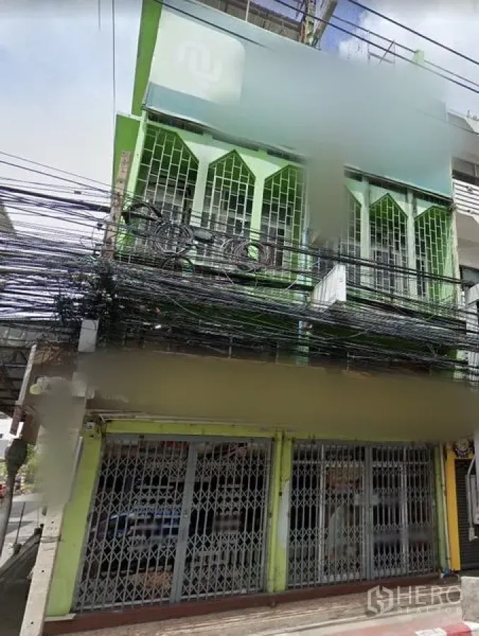 店屋 出租在Huai Khwang, Bangkok - Huai Khwang三层绿色店屋外观，一层金属折叠门，楼上带护栏阳台，临街位置人车流量旺。