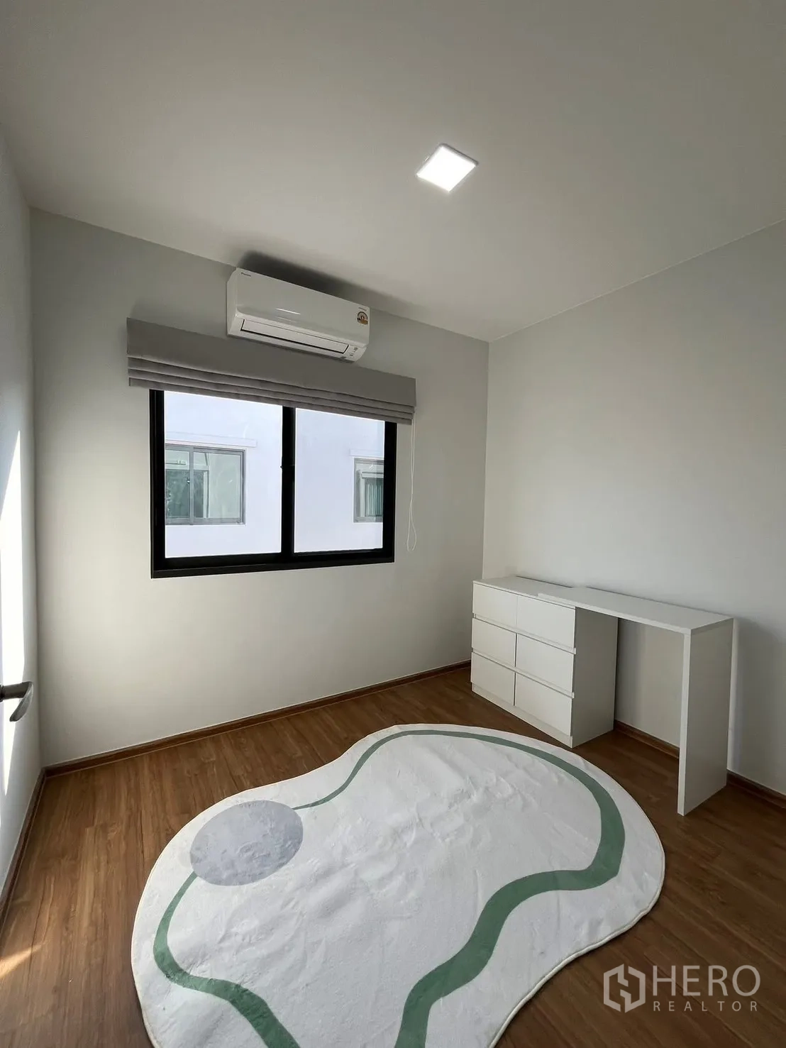 Townhouse for rent in Bang Phli, Samut Prakan - Bright bedroom with wood floor, air conditioner, window, and a white desk with drawers.