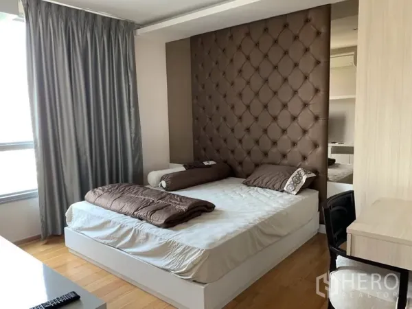 Condominium for rent in Watthana, Bangkok - Master bedroom with tufted feature wall, large bed, desk and floor-to-ceiling curtains.